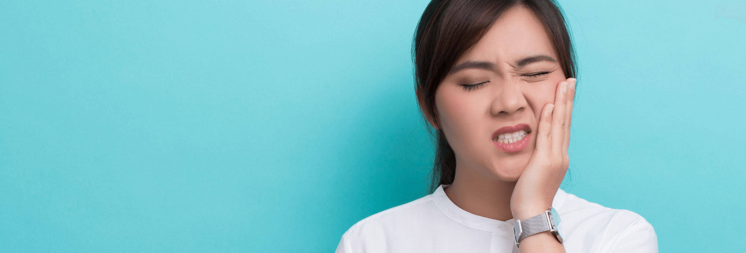 Asian woman with black hair and white blouse painfully holds her jaw